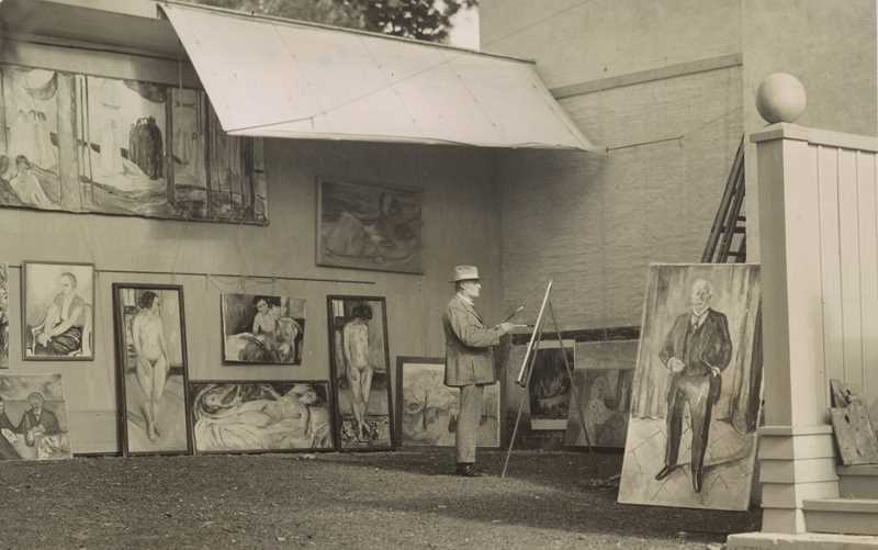Edvard Munch is standing and painting in his open-air studio at Ekely. He is surrounded by his own works and is wearing a hat to shield himself from the sun and a light-coloured suit.
