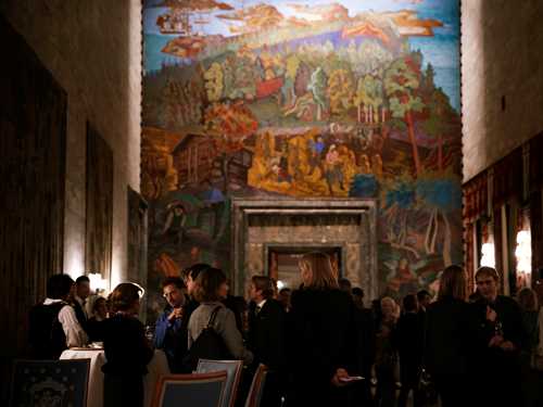 Sal i Oslo Rådhus. Mange mennesker står og snakker sammen og i bakgrunnen ser man et veggmaleri. Fotografi.