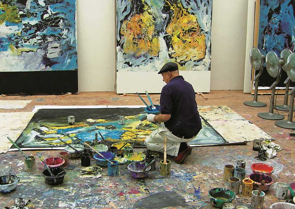 Foto av Georg Baselitc i atelier knelende ved maleri som ligger på gulvet.