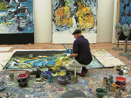 Foto av Georg Baselitc i atelier knelende ved maleri som ligger på gulvet.