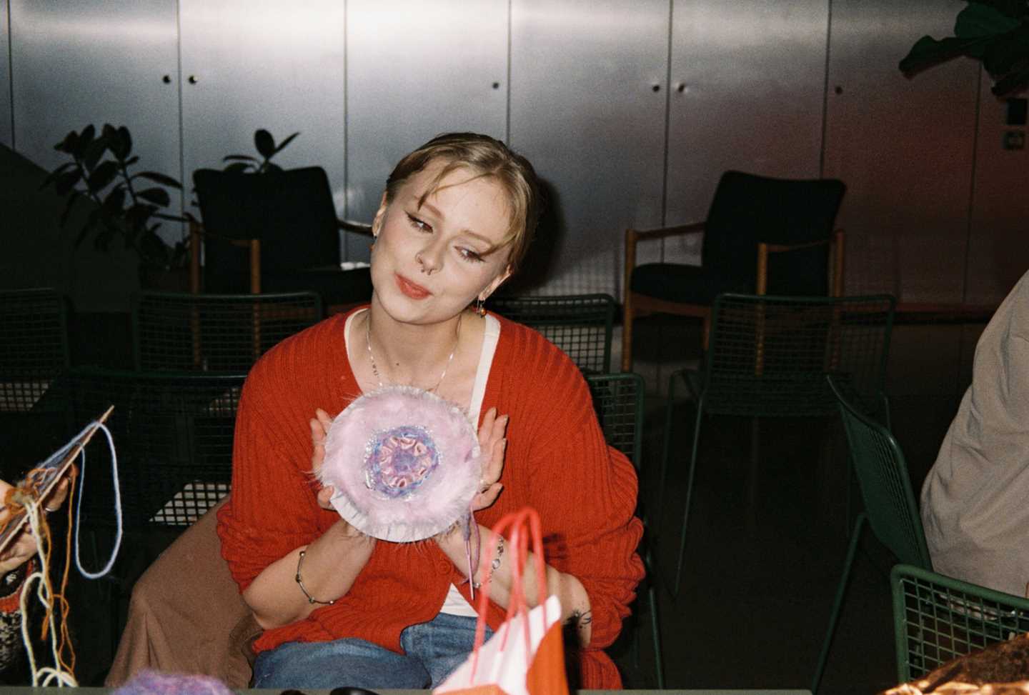 En jente i rød genser sitter og viser frem et håndarbeid hun har laget. Fotografi