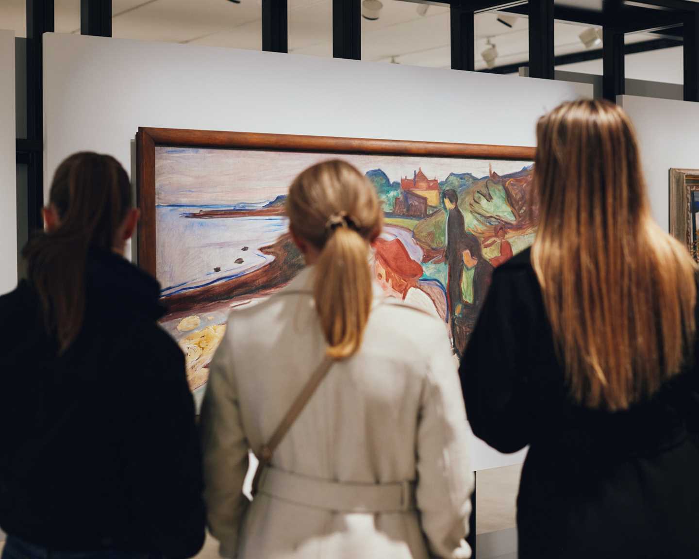 Tre kvinner med ryggen mot kameraet står og ser på et maleri av Edvard Munch. Fotografi