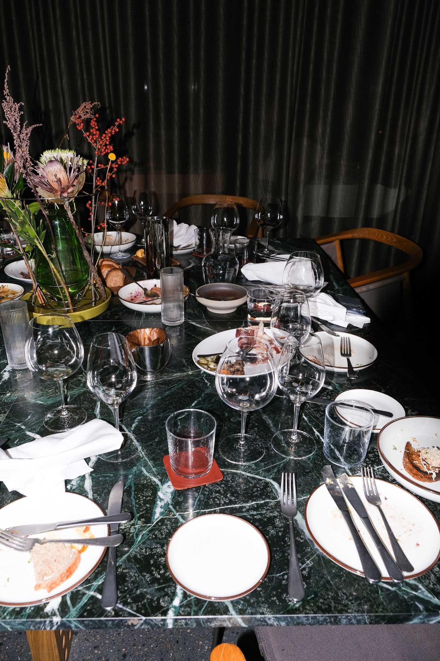 Et forlatt restaurantbord der brukte glass og tallerkner står igjen sammen med brukte servietter og stoler som er skjøvet ut fra bordet. Fotografi