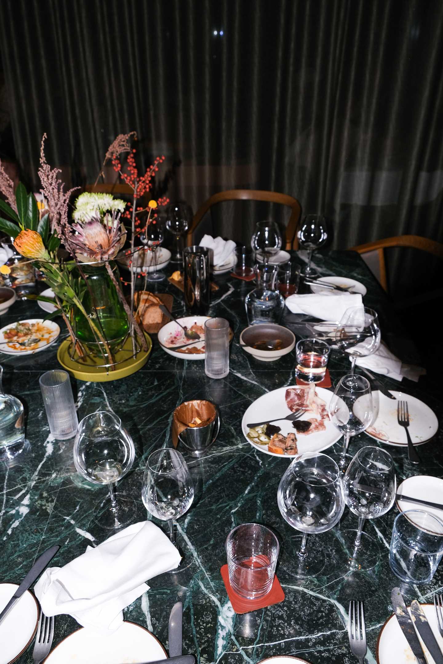 Et forlatt restaurantbord der brukte glass og tallerkner står igjen sammen med brukte servietter og stoler som er skjøvet ut fra bordet. Fotografi