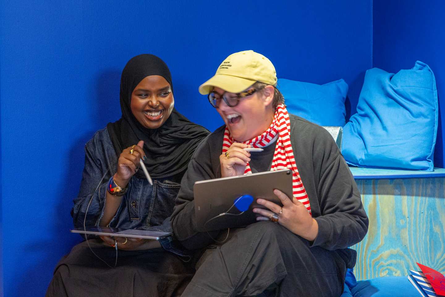 To jenter sitter med hvert sitt nettbrett og ler. Fotografi