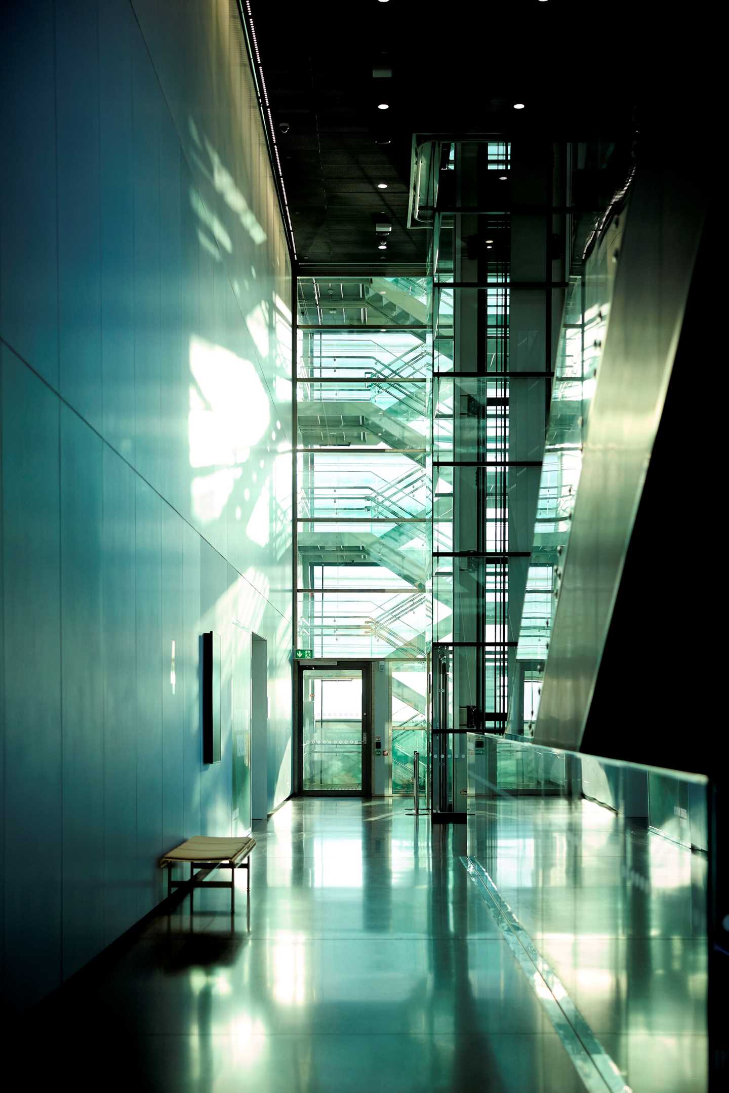 En av gangene på MUNCH der du ser en benk og en rulletrapp på hver sin side av gangsonen. I enden av bildet kan du se en trapp som går oppover i sikksakk. Fotografi