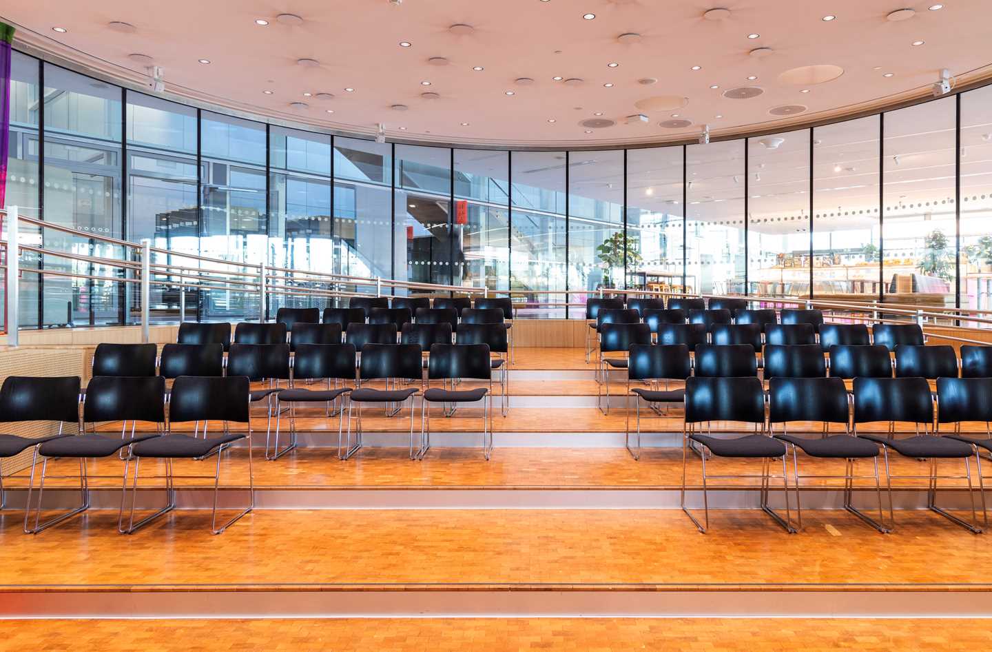 Amifet på MUNCH sett fra podiet nederst i amfiet. Det står fire stolrader med svarte stoler, skilt av en midtgang. Rundt hele rommet er det vinduer. Fotografi