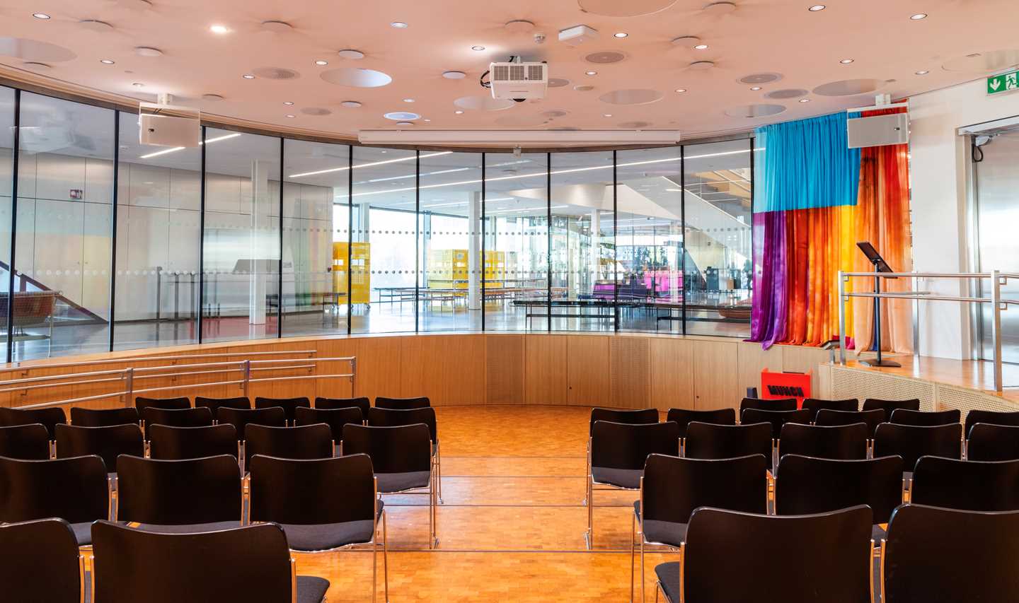 Amfiet på MUNCH sett fra den bakerste stolraden. Det står fire rader med svarte stoler på hver sin side av en midtgang. Fotografi