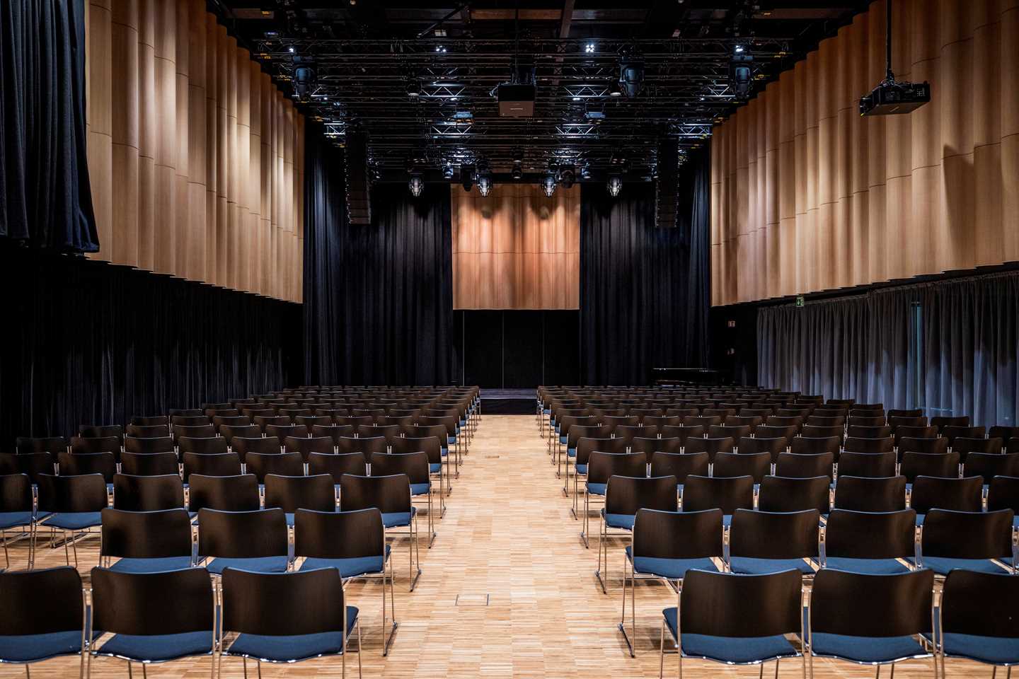 Festsalen på MUNCH sett fra bakerst i lokalet. Det er flere stolrader med svarte stoler som står foran en scene. Fotografi