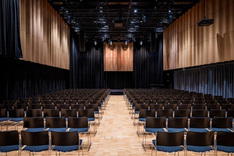 Festsalen på MUNCH sett fra bakerst i lokalet. Det er flere stolrader med svarte stoler som står foran en scene. Fotografi