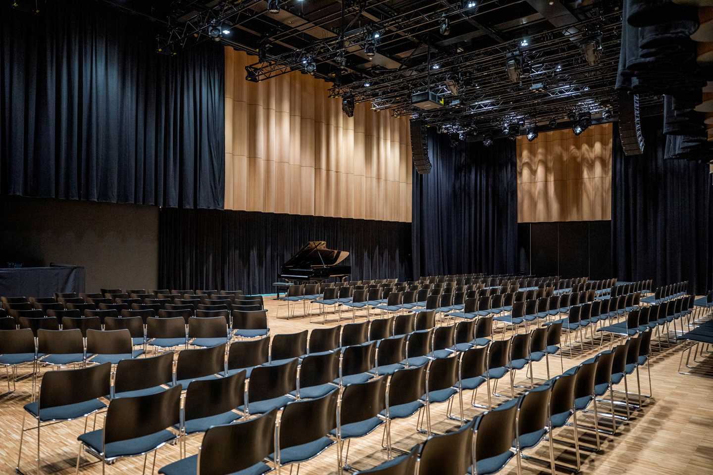 Festsalen på MUNCH sett fra høyre side. Flere stolrader med svarte stoler er rettet mot et flygel som står midt på salens ene langvegg. Fotografi