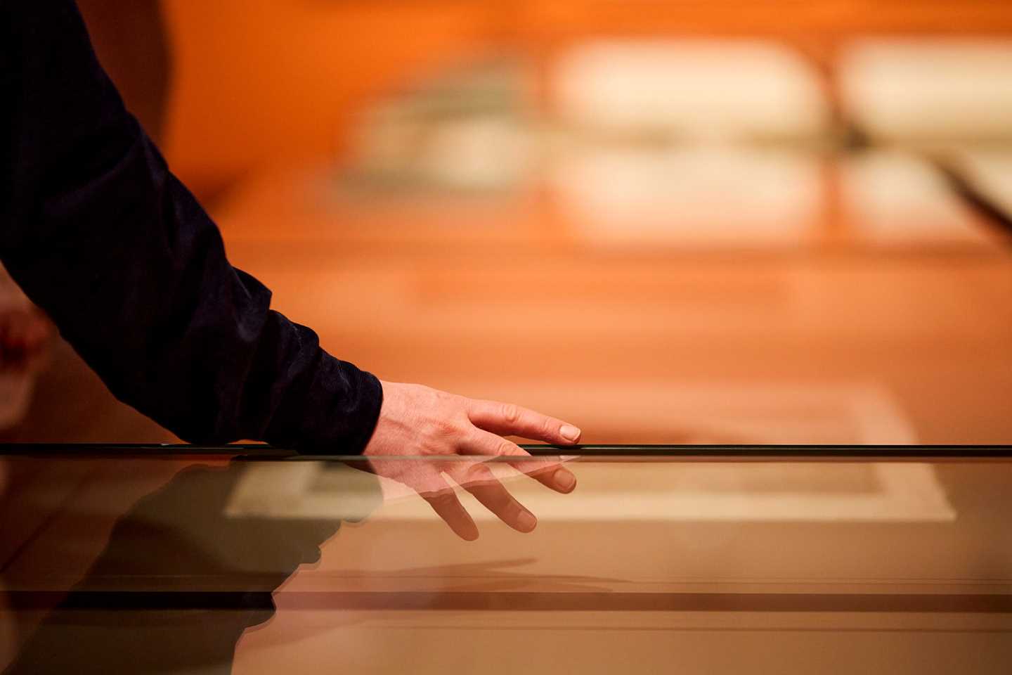 Nærbilde av en hånd som berører et glassmonter. Fotografi