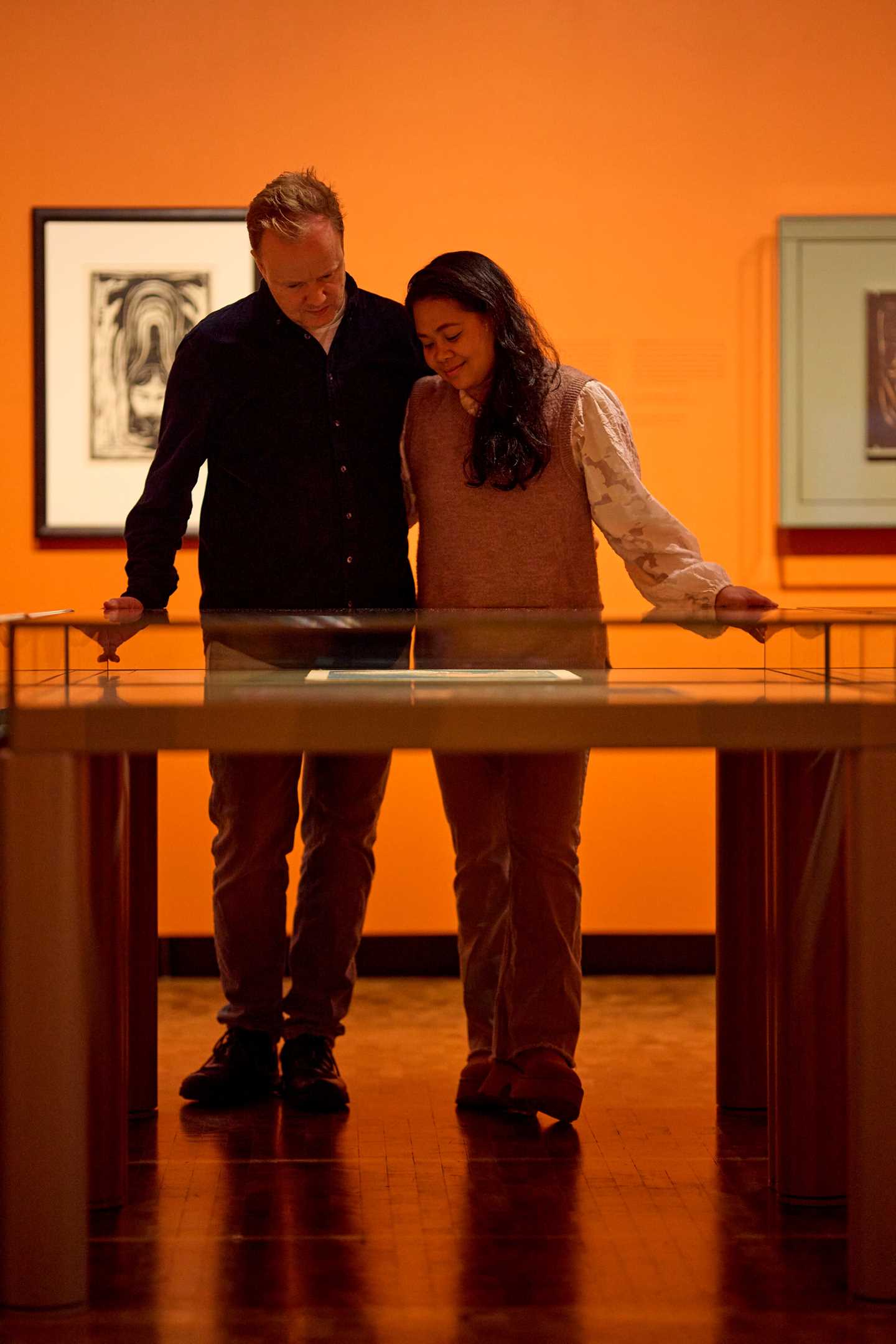 Et kjærestepar står og holder rundt hverandre mens de ser ned på et glassmonter med grafikk av Edvard Munch. Fotografi