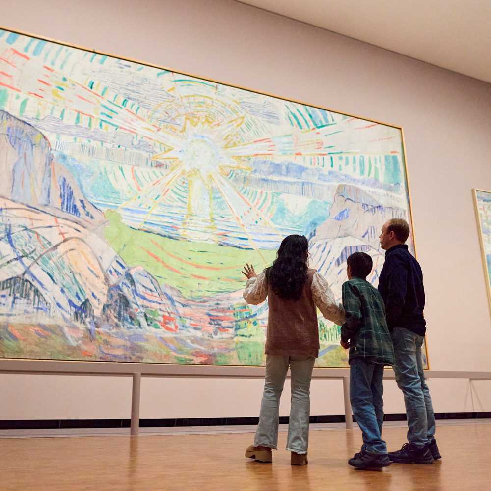 En mor, sønn og far står og ser på Solen av Edvard Munch. De står med ryggen mot kameraet. Fotografi