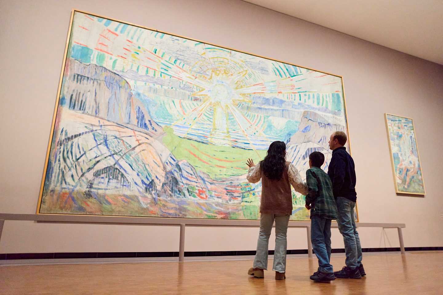 En mor, sønn og far står og ser på Solen av Edvard Munch. De står med ryggen mot kameraet. Fotografi