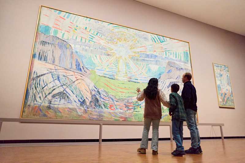 En mor, sønn og far står og ser på Solen av Edvard Munch. De står med ryggen mot kameraet. Fotografi
