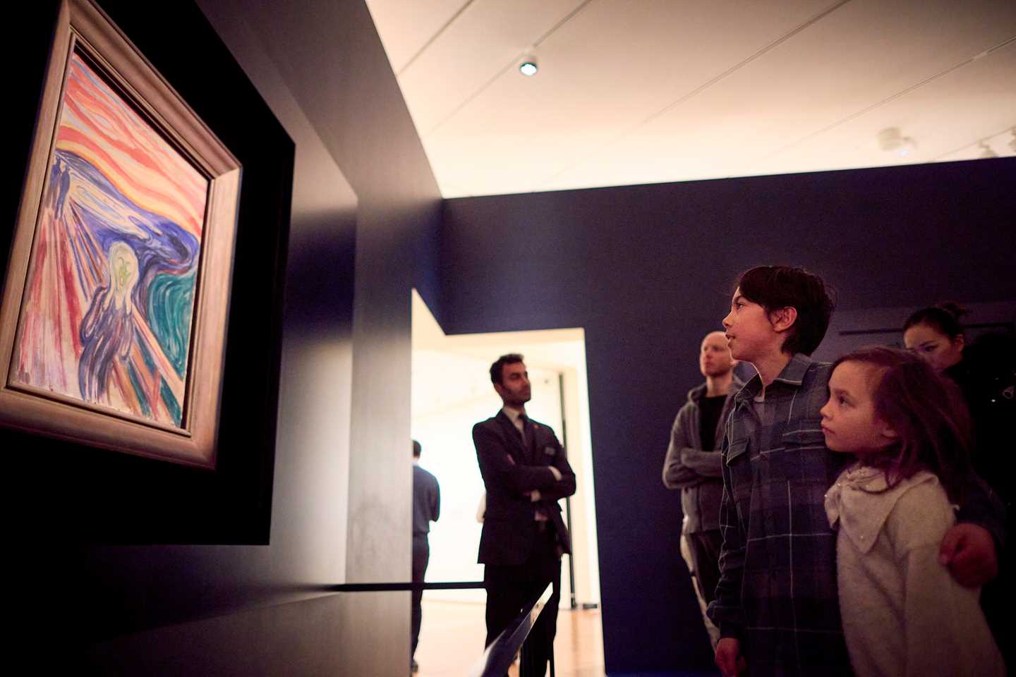 En familie på fire står og beundrer Skrik av Edvard Munch. I bakgrunnen står en vakt og passer på verket. Fotografi