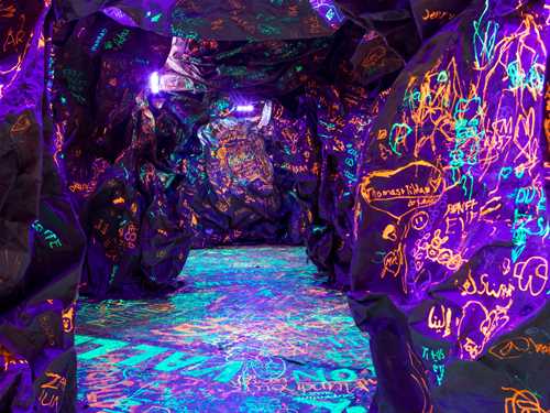 En knudrete, mørk hule der barn og voksne har skriblet med selvlysende blekk. Fotografi