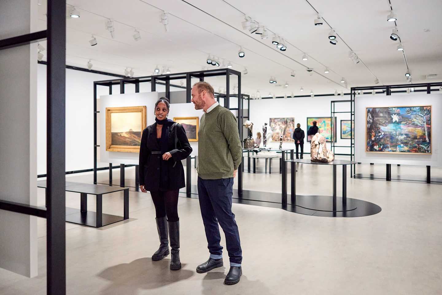 To personer står i et utstillingsrom og betrakter et kunstverk. Fotografi