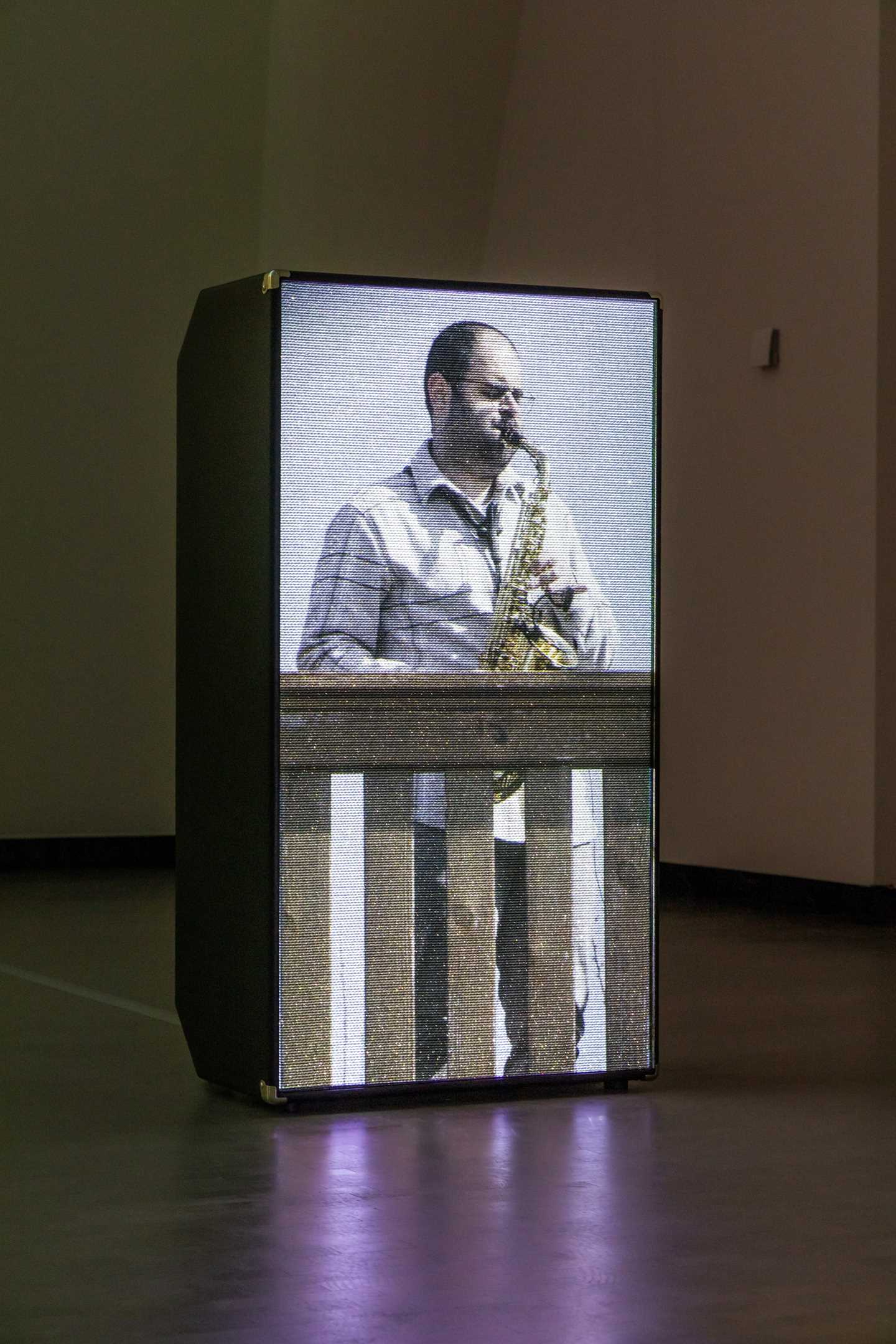 En projeksjon av saksofonisten Amr Mdah, som spiller mens han står på en balkong, vises på en høyttaler. Fotografi