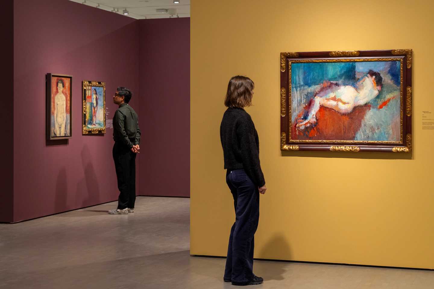 To mennesker ser på verk av Ludvig Karsten. Nærmest kamera ser en kvinne på verket Liggende akt. Fotografi