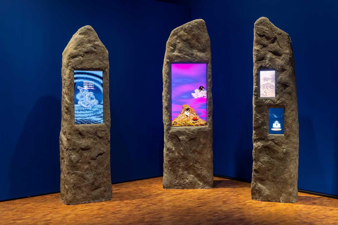 ChatGPT said: Three boulders have embedded screens showing different clips in vivid colours. Photograph.
