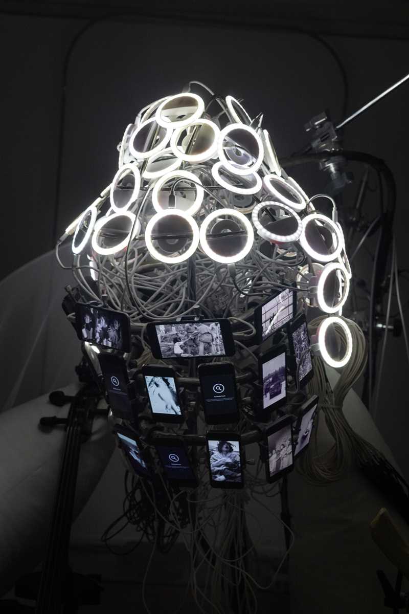 Circles of white LED lights, wires, and mobile phone screens are assembled into the shape of a Buddha head. This is a close-up of part of the installation. Photograph.
