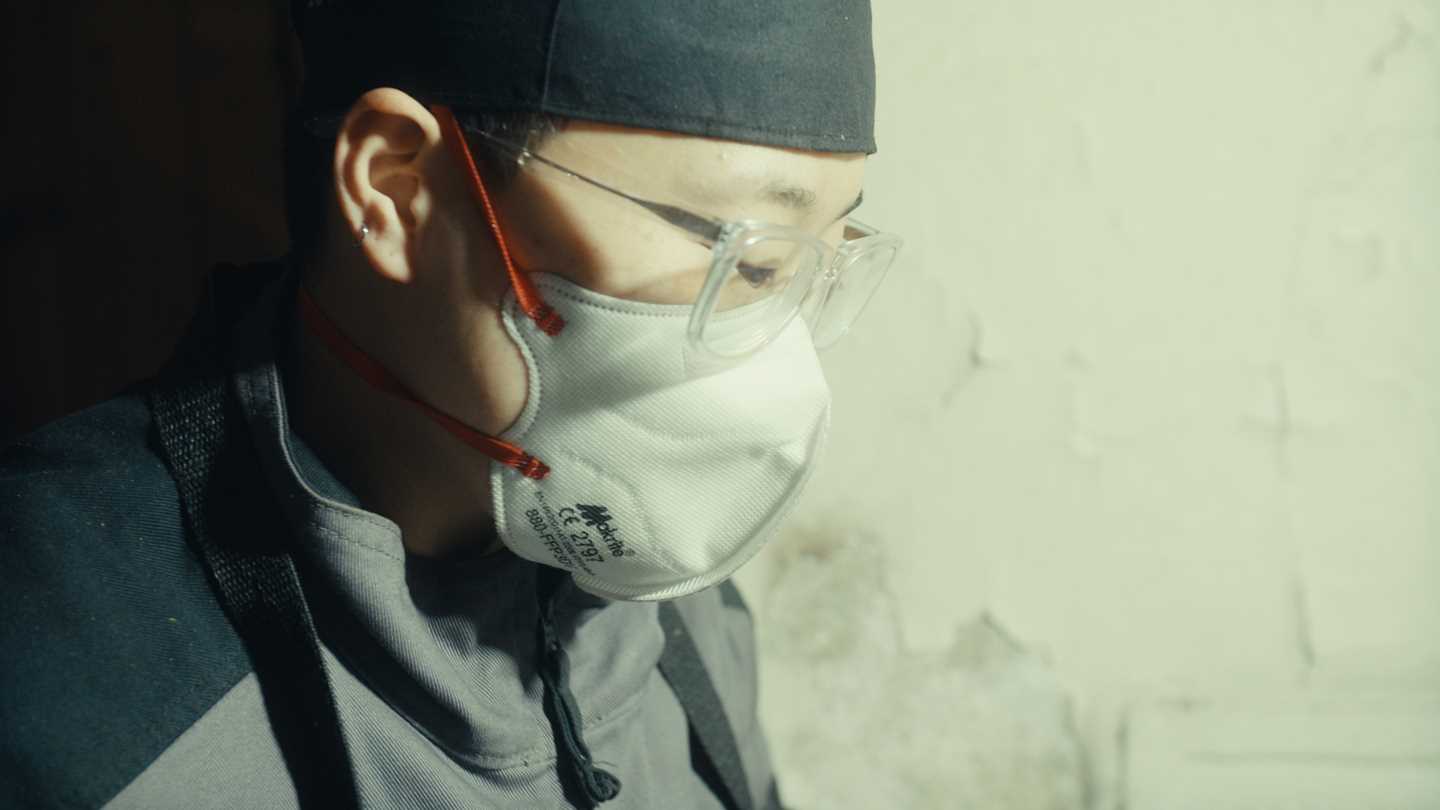 Close-up profile of artist Kim Hankyul wearing a black head covering, glasses and a white face mask. Photograph.