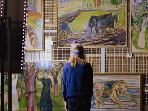 Artist Marie Ulven står med ryggen mot kamera foran flere verk av Edvard Munch. Fotografi