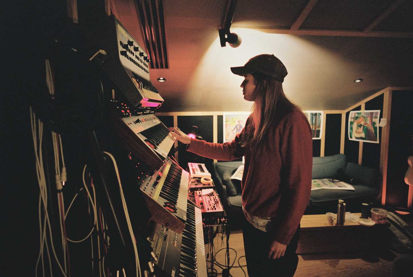 Artist Marie Ulven står ved en vegg der det henger flere keyboard nedover veggen under hverandre. Hun spiller på tangentene på ett av keyboardene. Fotografi