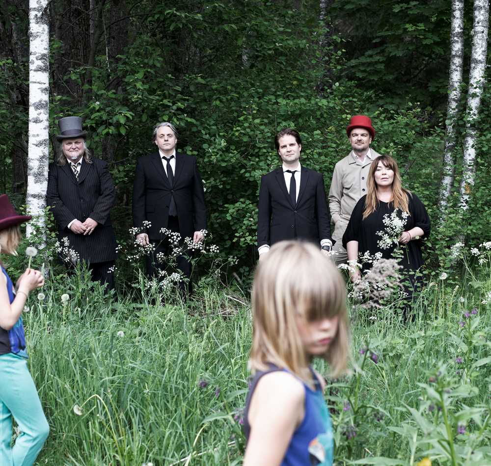 Foto av bandmedlemmer stående i en skoglysning med barn i forgrunnen.