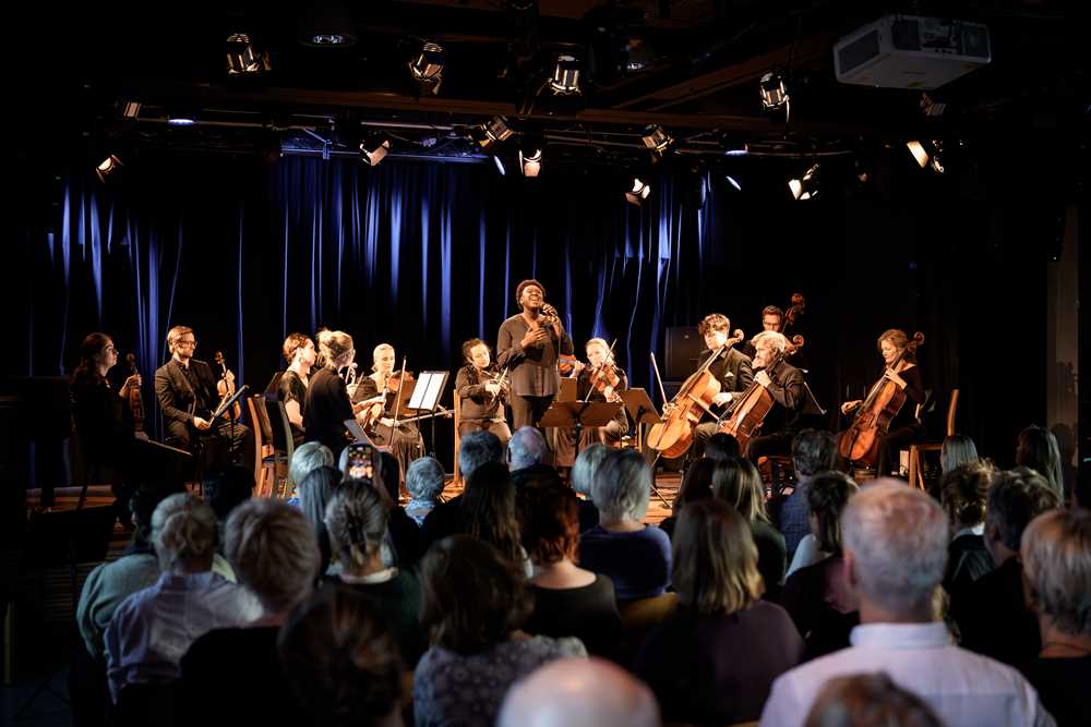 Foto av bandmedlemmer i konsert på scenen med publikum i forgrunnen.