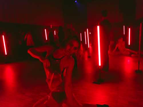 Mennesker i klær av gjennomsiktig plastikk beveger seg rundt i et mørkt rom lyst opp av røde lysrør.