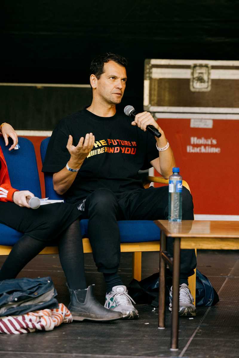 Performancekunstner Manuel Pelmus sitter på scenen og snakker i en håndholdt mikrofon. Fotografi
