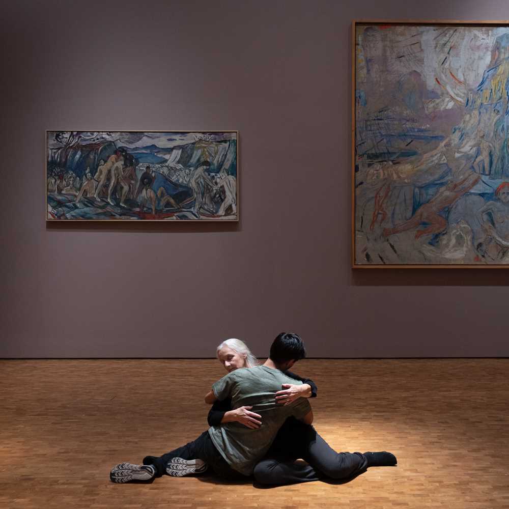 To mennesker sitter på gulvet i en omfavnelse. I bakgrunnen ser du maleriet Menneskeberget av Edvard Munch. Fotografi